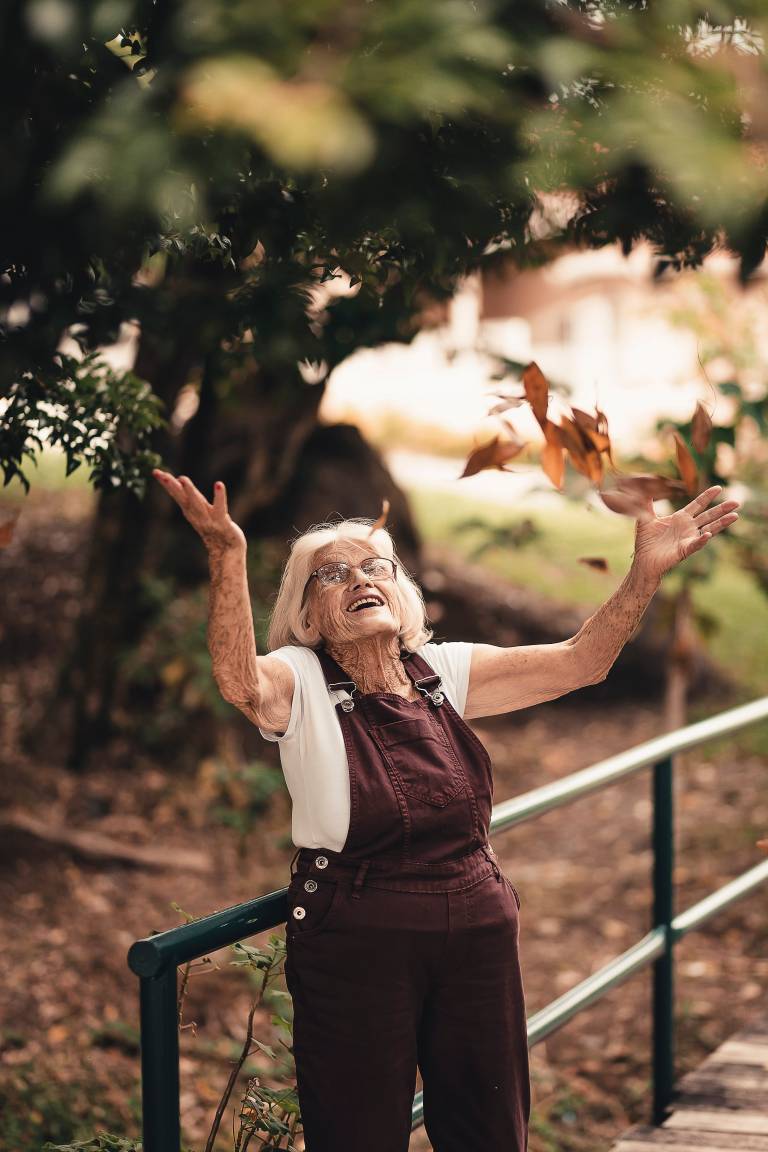 Older woman throwing pile of leaves into air with smile on her face