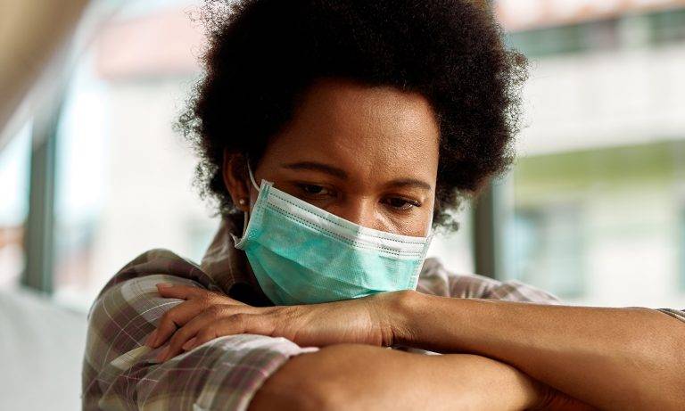 Image of a stressed woman wearing a surgical mask with her arms crossed