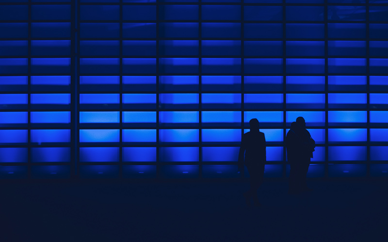 Two people silhoutted against an abstract blue screen with many blocks, representing patterns and data