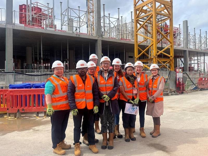 a group of people in hi vis jackets in front of the two-story concrete structure of Oriel which is under construction