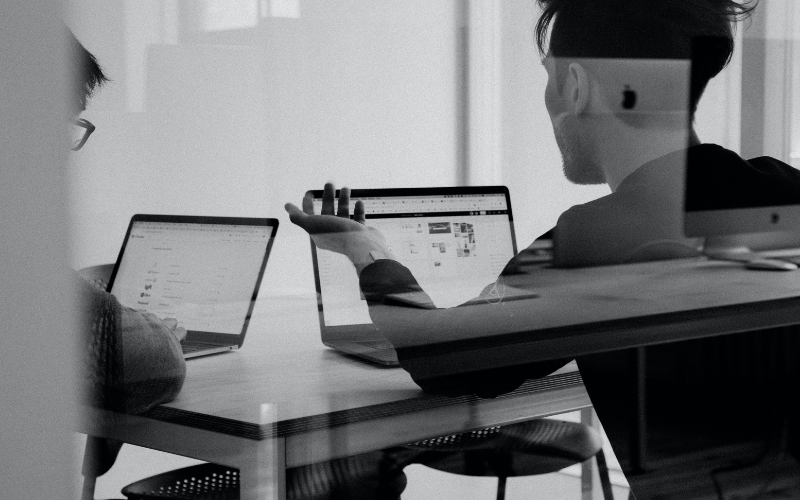A black and white image of two people having a discussion at their desks