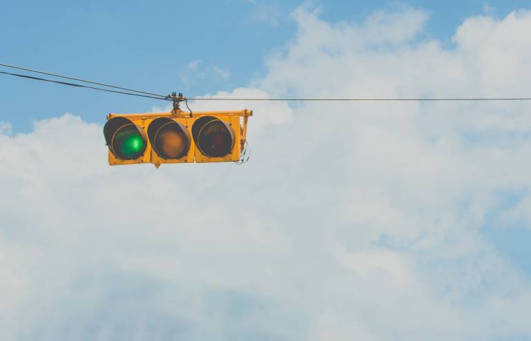 A photo of a green traffic light suspended against a blue sky