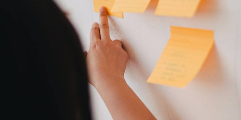 An arm is shown sticking a sticky note onto a board as part of a brainstorming session