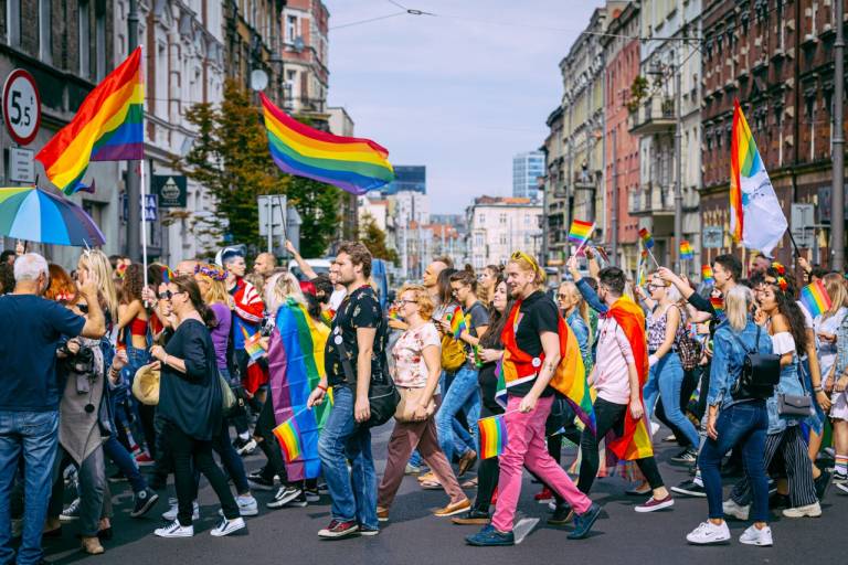A group of marchers in a Gay Pride march in Poland crossing a street. Many are carrying or wearing rainbow flags.