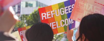 A photo taken at a march, focus is on a rainbow sign reading Refugees Welcome