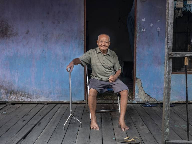 An older man sitting on a chair in front of a house.