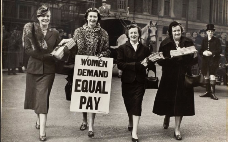 four women in a black and white photo holding a sign that says 'women demand equal pay'