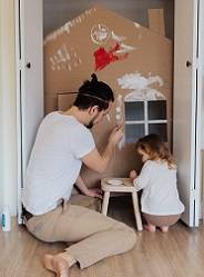 Photo of man and toddler painting a cardboard house