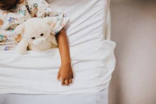 Child in bed, holding a teddy bear