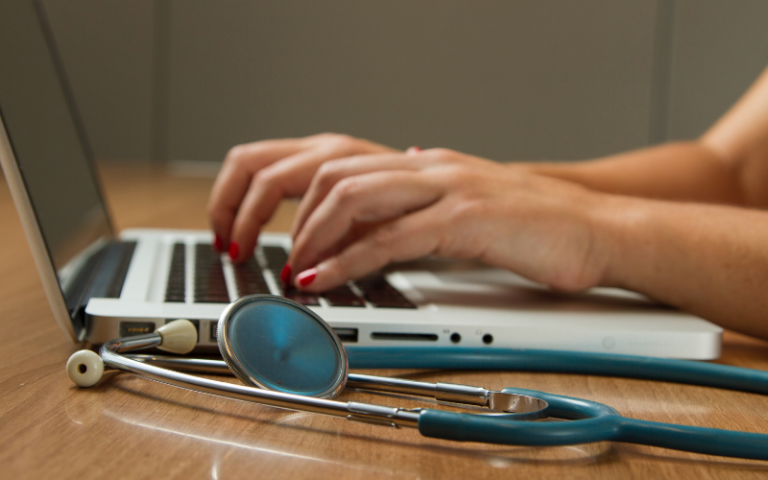A person's hands using a laptop next to a stethoscope