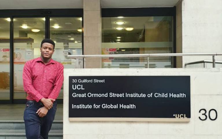Student leaning against a building sign that reads 'UCL Great Ormond Street Institute of Child Health, Institute for Global Health, UCL'