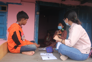 A hearing impaired boy sits with a researcher outside his house with a sign language translator in rural Nepal.