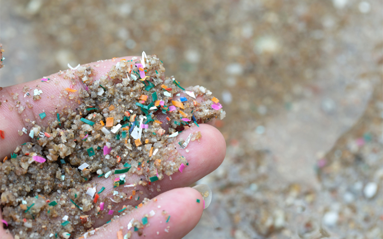 Close-up side shot of hands shows microplastic waste contaminated with the seaside sand