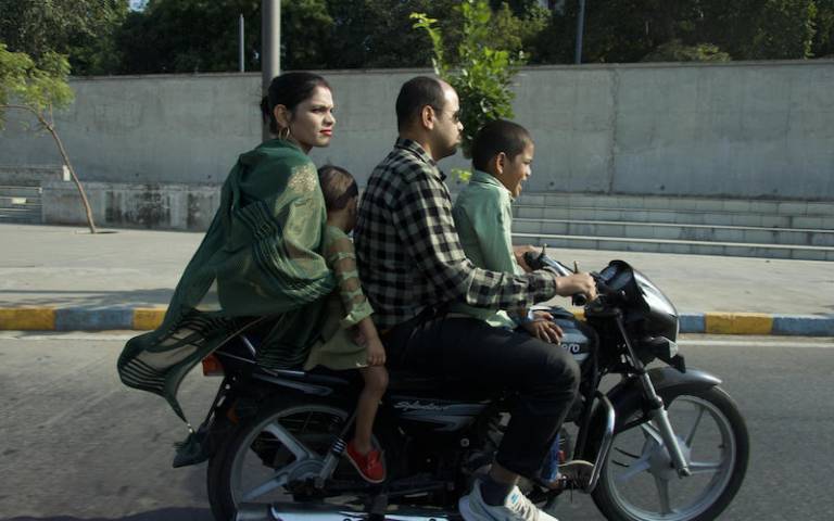 woman in green sari on the back of a motorbike with husband and two children