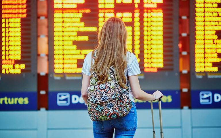 female student standing in front of departures board at airport