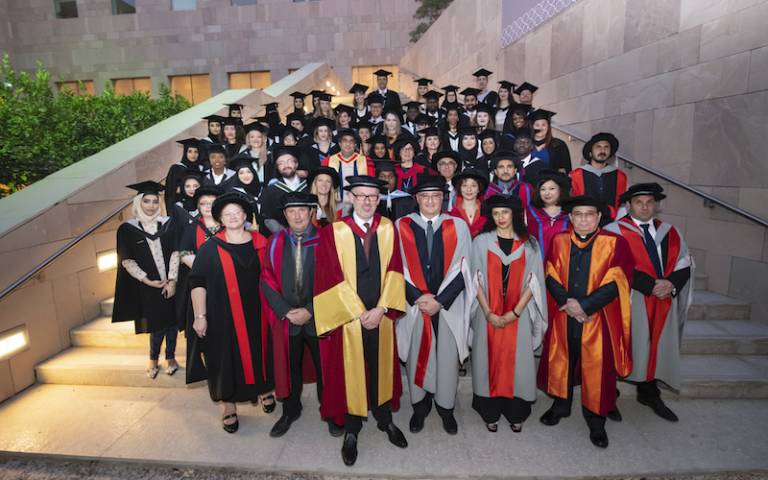 UCL Qatar graduates on steps in their caps and gowns