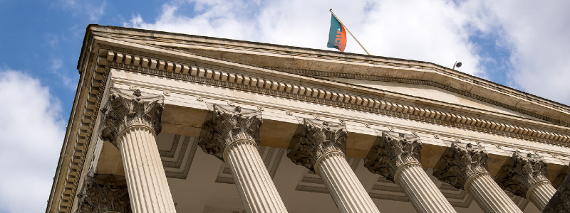 Image of the UCL Portico building flying a blue and orange UCL flag.