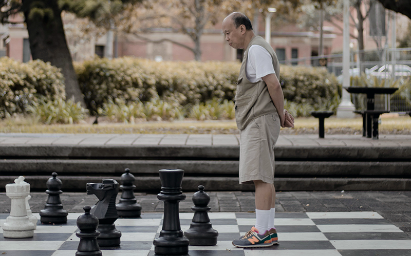 an image of an elderly man playing with a giant chess set 