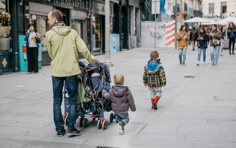 A young father walks with his young children along a city street.