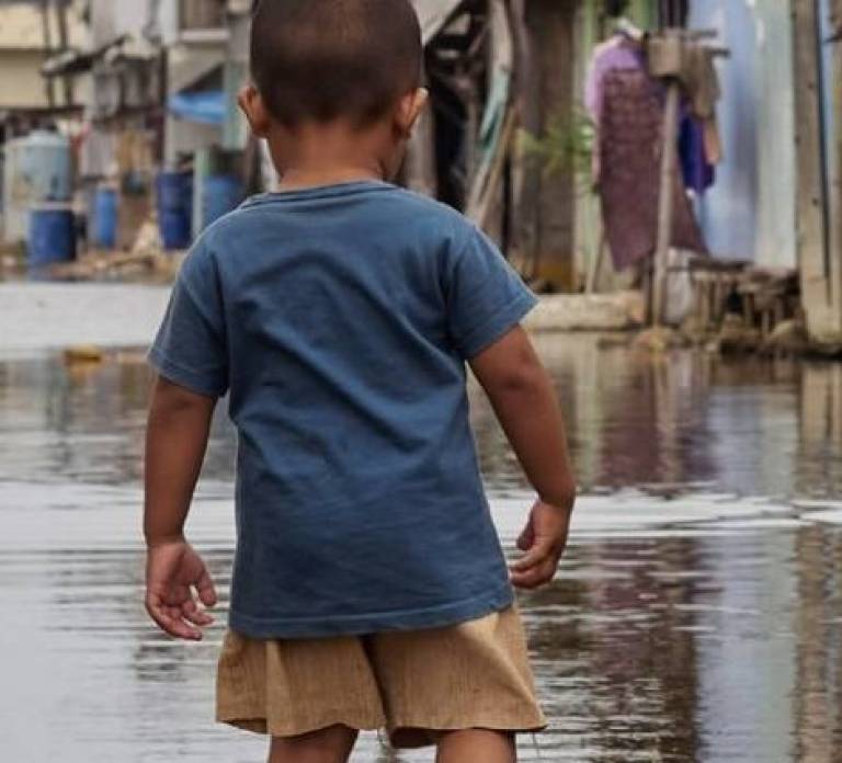 A young boy stands in water which has flooded the street and is up to his knees