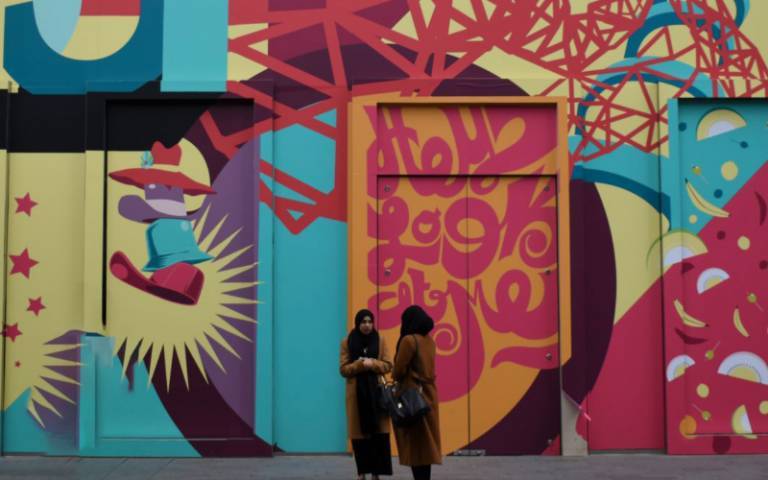 Two women stand on an urban street in front of a mural