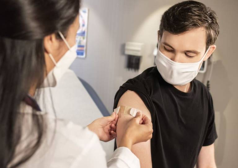A young person is having a plaster put on his arm having just received a jab from a doctor. Both people are wearing masks.