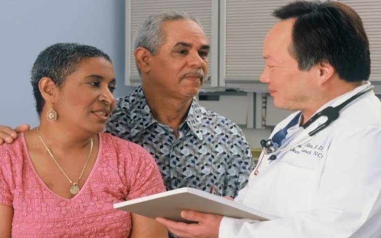Doctor in white lab coat and stethoscope discusses results with couple