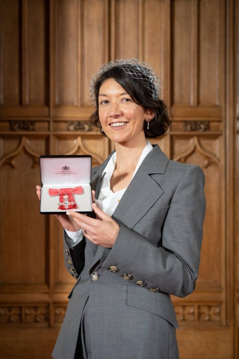 Pictured Professor Laura Shallcross, in a grey suit, holds the MBE medal for her national contributions to the COVID-19 efforts.