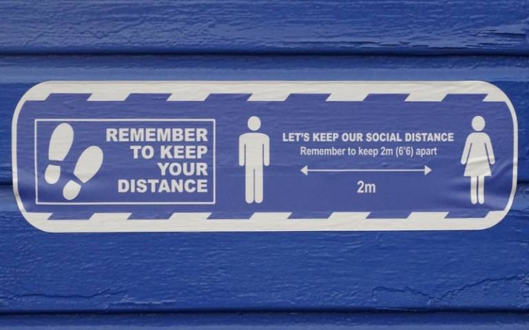 A blue sign on a blue wall reminds people to keep 2m distance between other people during the covid-19 pandemic