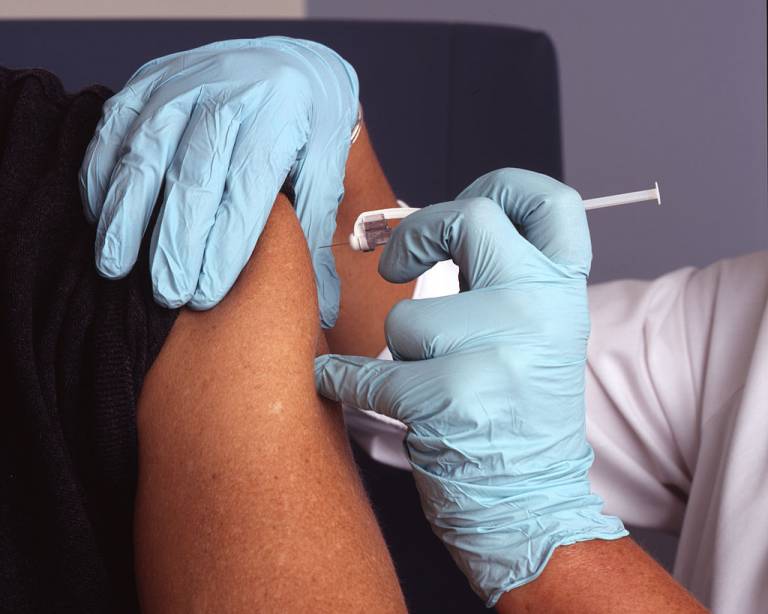 A nurse wearing blue gloves administers a vaccine into a male patient's arm.
