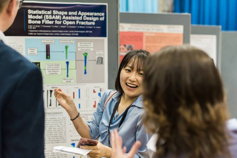 A research student smiling whilst showing her poster