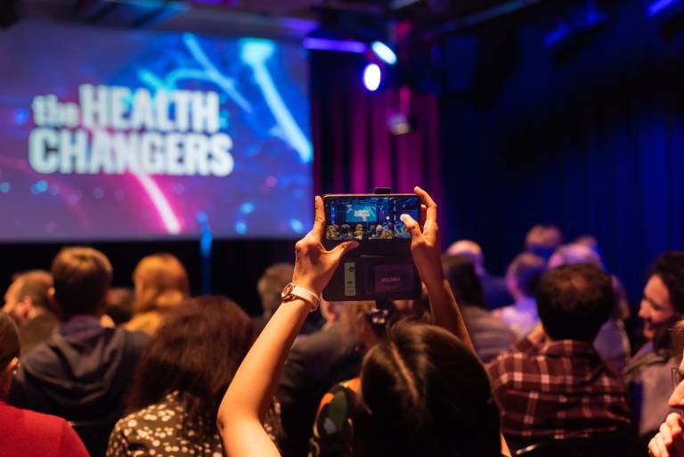 Image of a woman holding her phone up as she takes an image of the 'health changers' background image