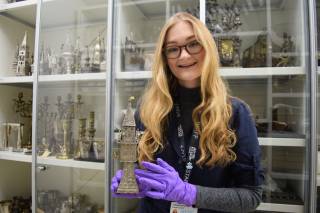 photo of Jemima Jarmon holding Jewish artifact in front of a cabinet of artifacts at a museum