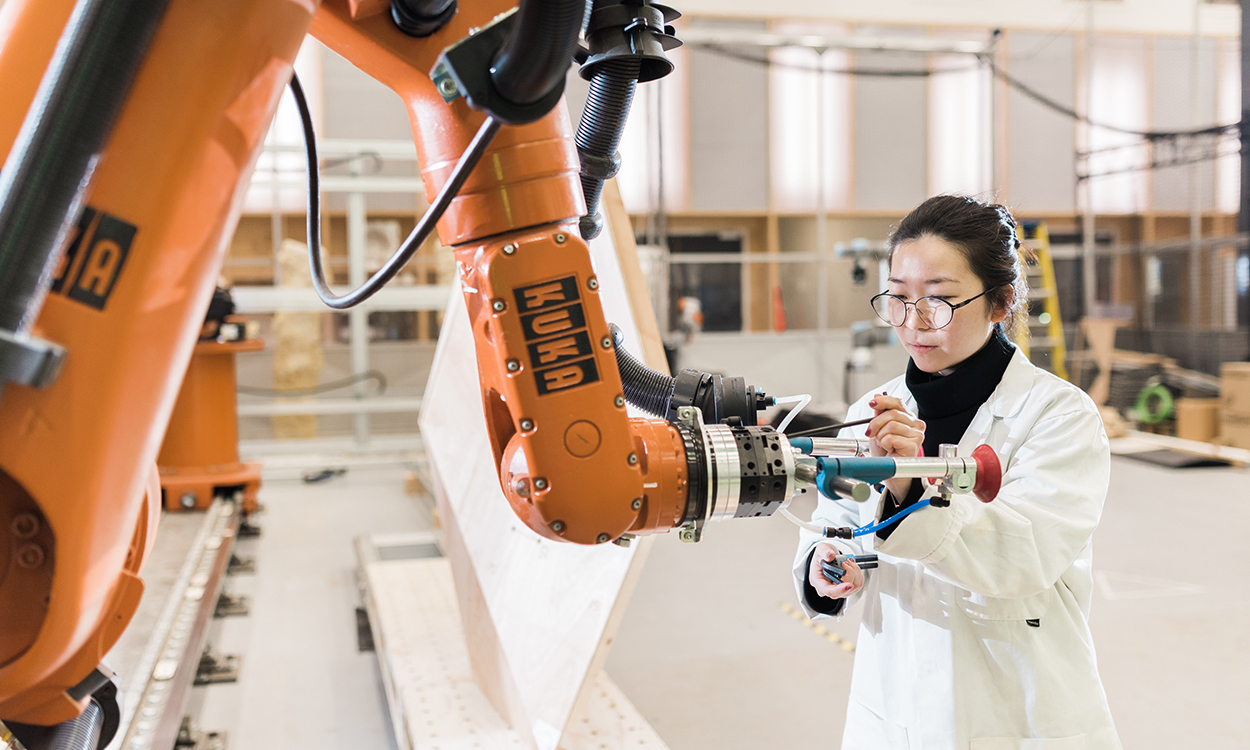 woman in lab coat works with large robot arm