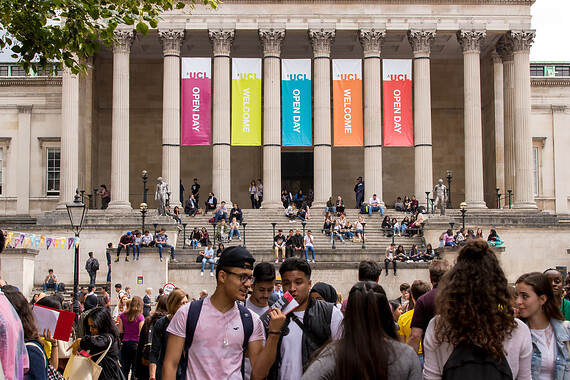 Students in the foreground, more students in groups on the steps to main entry, colourful banners hanging from the colonnade reading Open Day and Welcom 