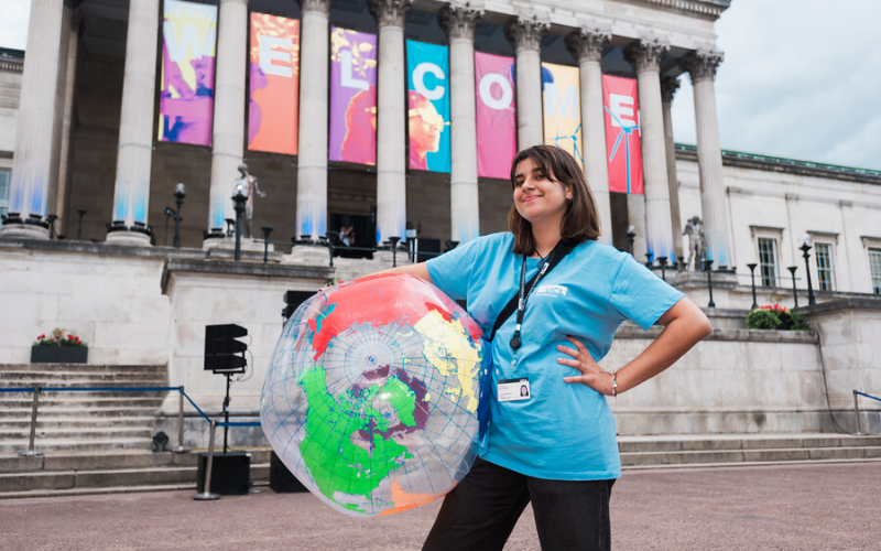 UCL student stands with a globe in front of main campus at welcome
