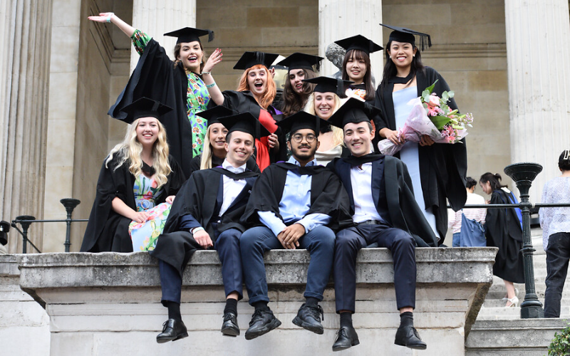 UCL Graduate students sit on the wall at main campus celebrating