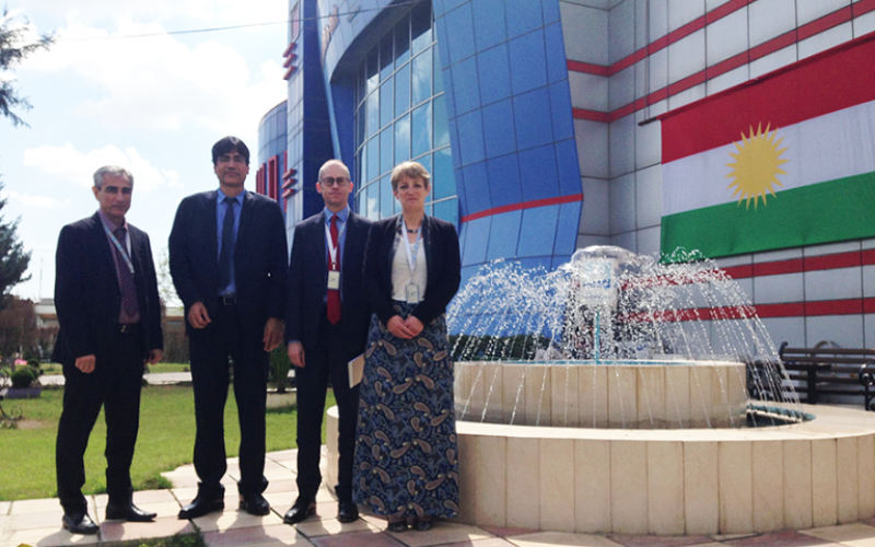 Eleanor Robson of UCL History and delegates stand in front of waterfall at Kurdistan flag front