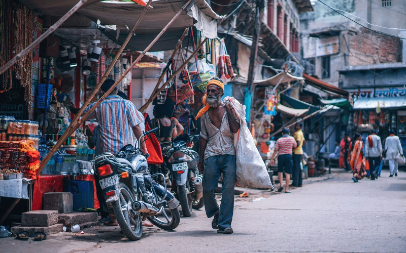 man walks through street in south asia next to motorcycle holding a white plastic bag