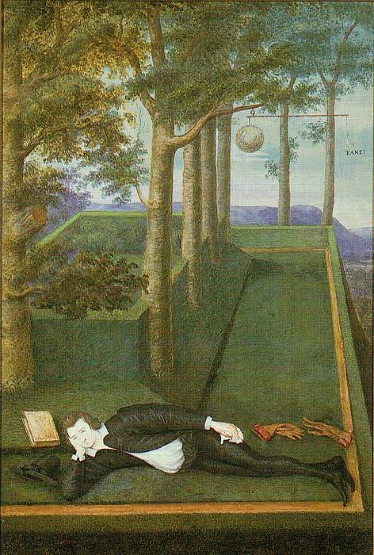 a man lies on the floor with trees behind him. he is wearing a white shirt and a black jacket and trousers