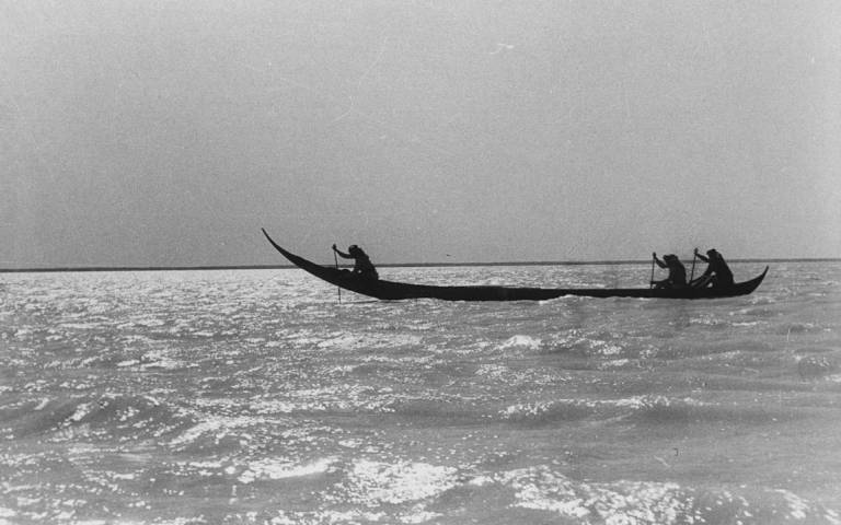 Black-and-white image of the tarada canoe, manned by three oarsmen, floating on a river