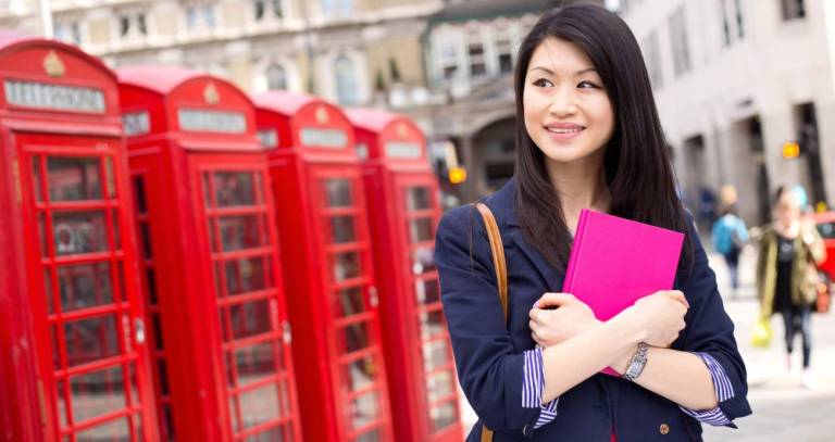 Student holding a pink notebook in front of London phoneboxes