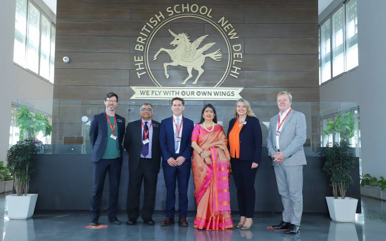 6 people stand in front of The British School New Delhi Logo