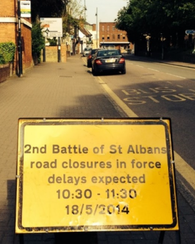 Yellow road sign on a quiet street in St Albans - it says 2nd battle of st albans road closures in force delays expected