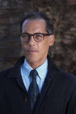 a man in glasses, wearing a shirt and tie looks at the camera