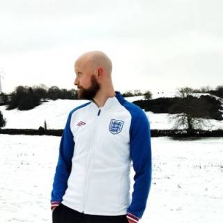 A bald white man with a beard looks to the left with a snowy background behind him