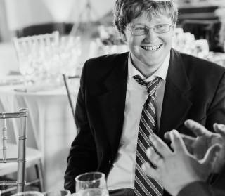 A young man in a suit and glasses smiles to someone on the right