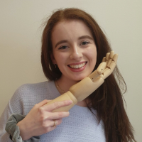 Lucy Dowdall Smiling At Camera Holding A Wooden Hand