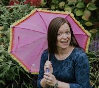 Sarah White Holding a Pink and Yellow Umbrella, Smiling at the Camera