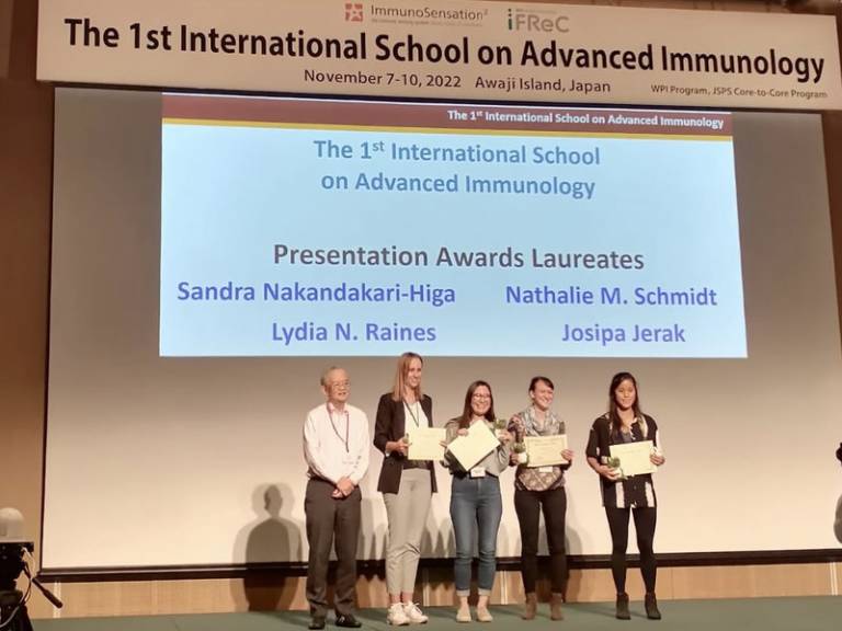 Some visiting delegates receive awards on a stage at the First International School on Advanced Immunology. Projector screen in the background.